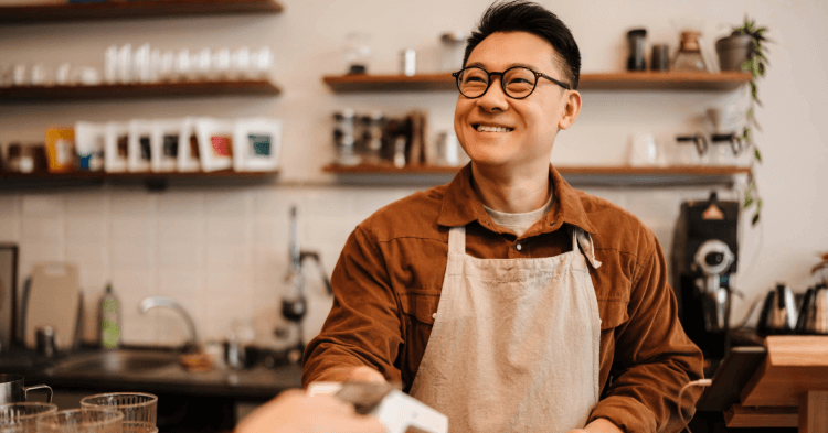 Male cafe owner smiling as he recieves a credit card payment.